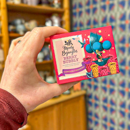 Een hand houdt een felroze doosje met Monty Bojangles Berry Bubbly chocoladetruffels vast. 