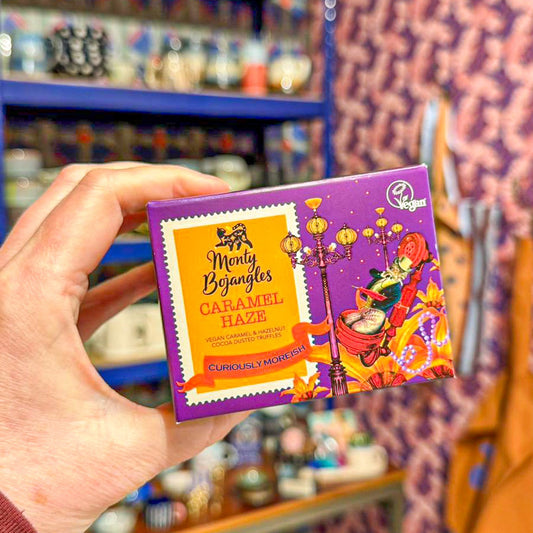 Op de foto staat een doosje met Monty Bojangles chocoladetruffels in de smaak Caramel Haze. Het doosje is paars met gele en oranje details.