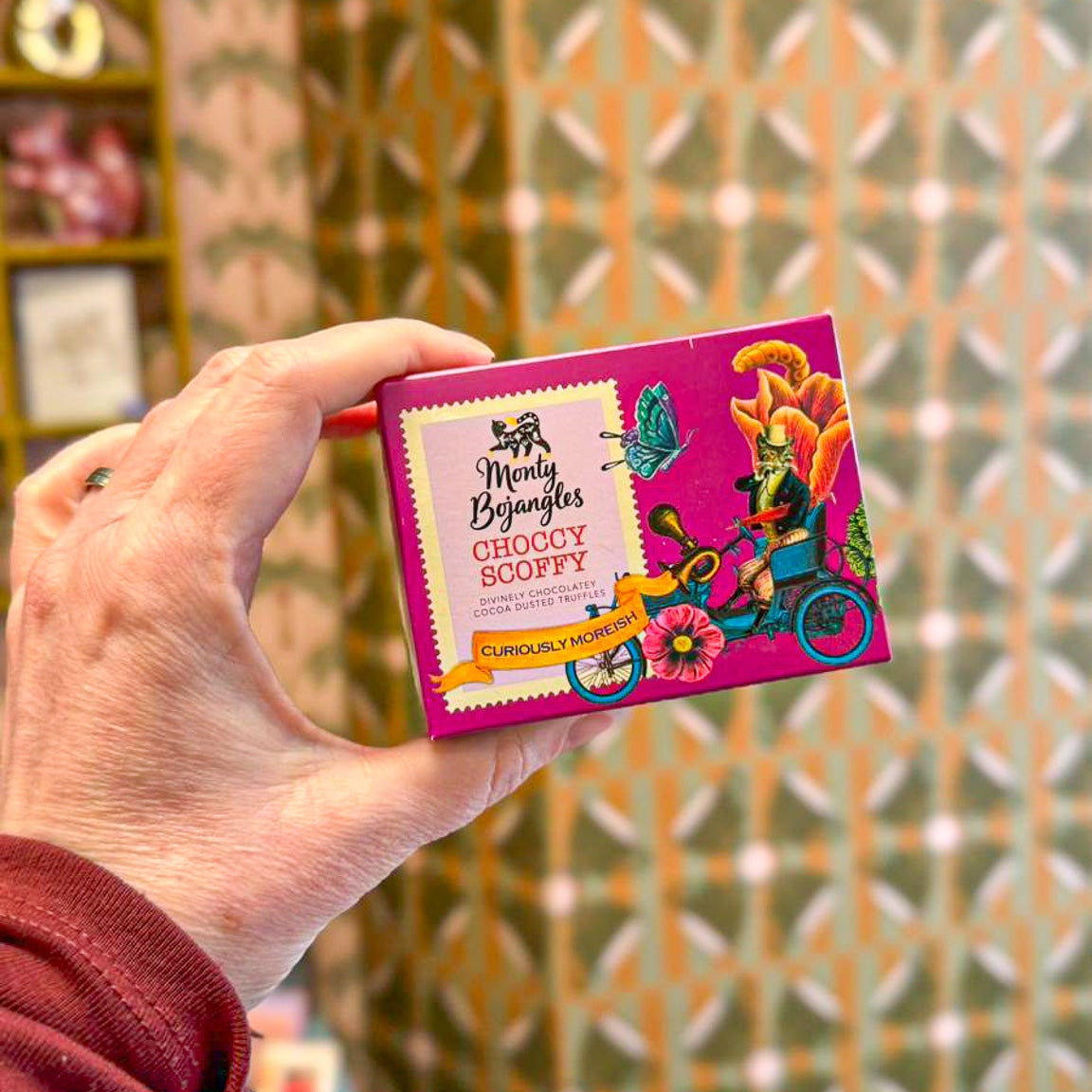 Een hand houdt een doosje vast met Monty Bojangles Choccy Scoffy chocoladetruffels.