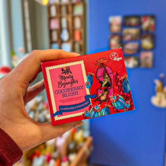 Een knalroze doosje met Monty Bojangles in de smaak Cocoberry Blush wordt vastgehouden door een hand. 