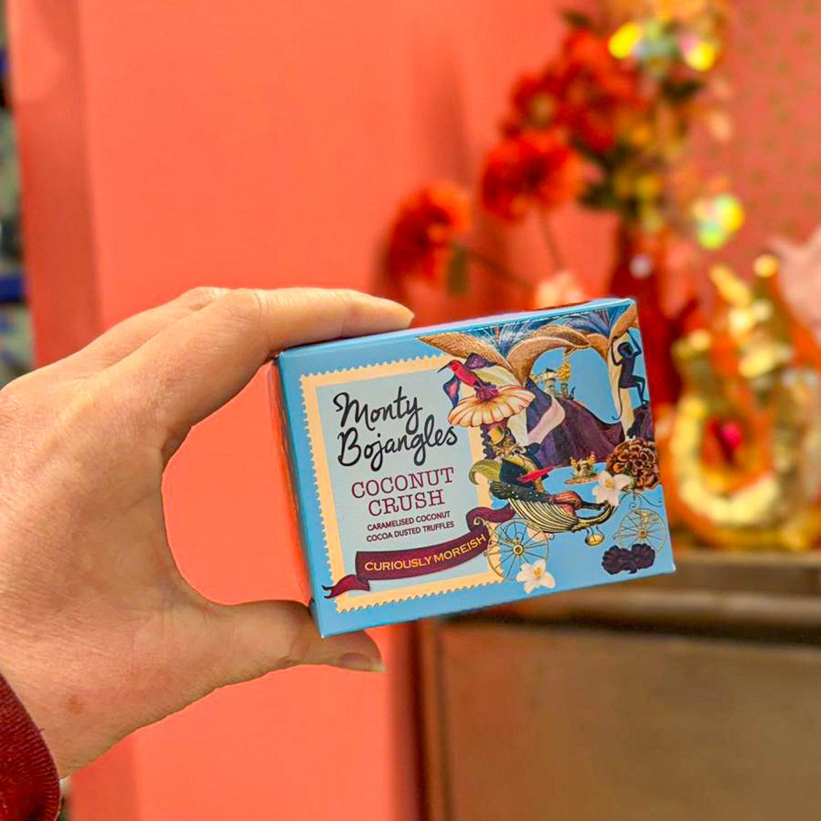 Op de foto zie je een hand die een lichtblauw doosje Monty Bojangles vasthoudt. De chocoladetruffels zijn in de smaak Coconut Crush. 