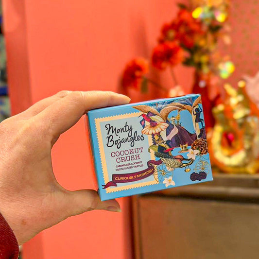 Op de foto zie je een hand die een lichtblauw doosje Monty Bojangles vasthoudt. De chocoladetruffels zijn in de smaak Coconut Crush. 