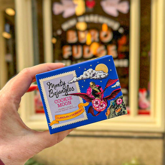 Een hand houdt een kobaltblauw doosje vast met Monty Bojangles chocoladetruffels in de smaak Cookie Moon.