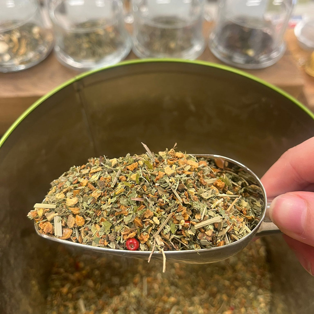 Een maatschepje met losse thee boven een groen theeblik.