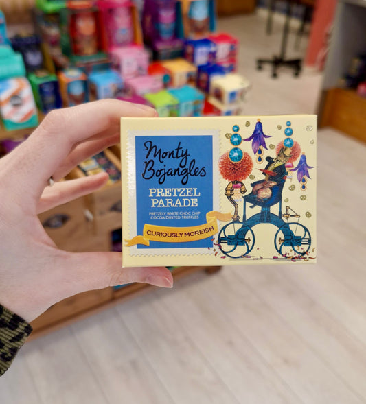 Een hand houdt een lichtgeel doosje vast met daarin Monty Bojangles Pretzel Parade chocoladetruffels.