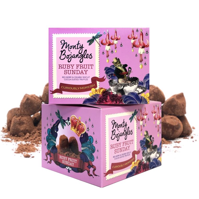 Op de foto staan twee doosjes van de Monty Bojangles in de smaak Ruby Fruit Sunday. De doosjes zijn lichtroze. Achter de doosjes liggen wat chocoladetruffels.