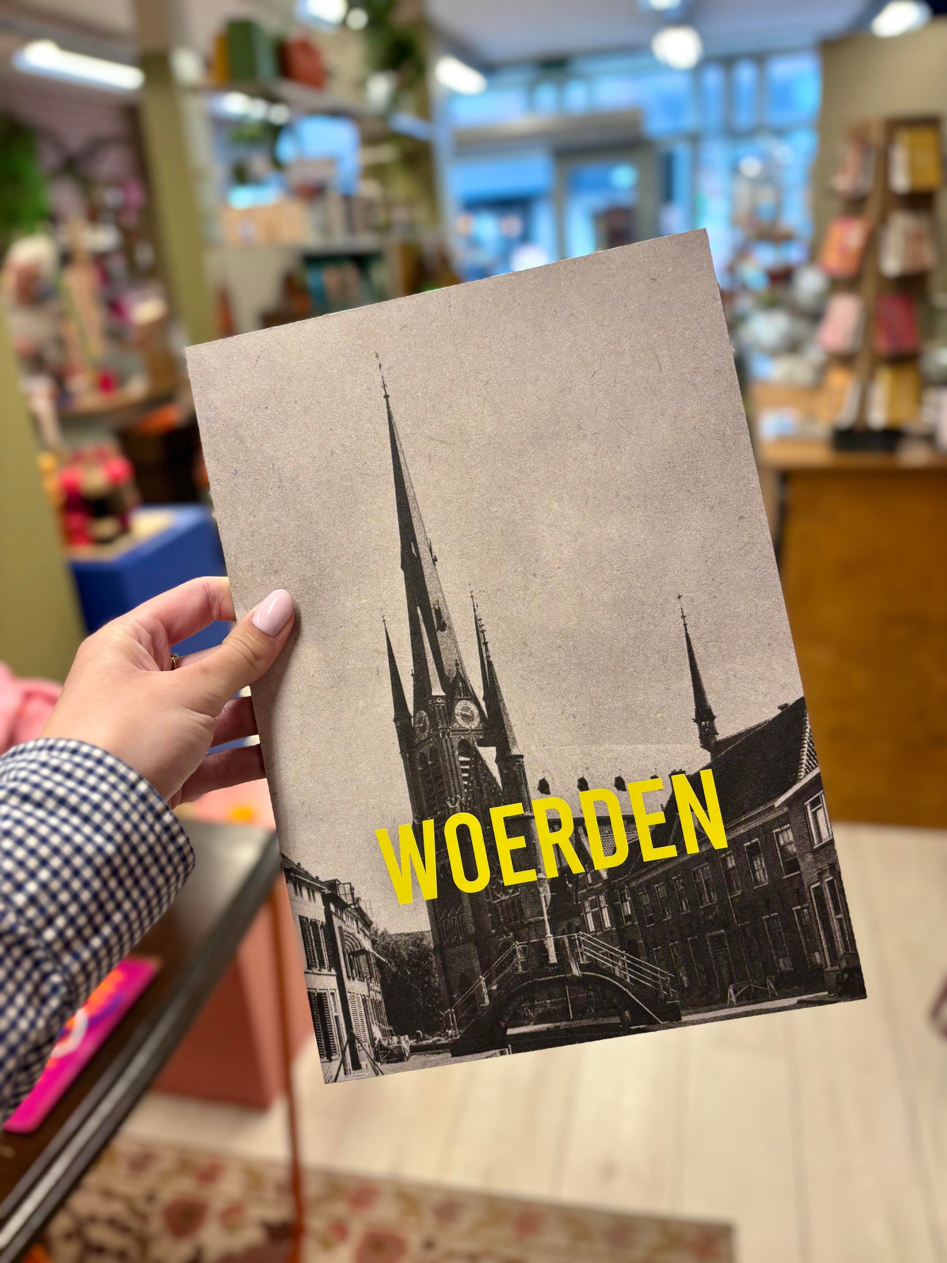 Op de foto zie je een hand die een poster vasthoudt met daarop en kerk en in gele letters 'Woerden'.