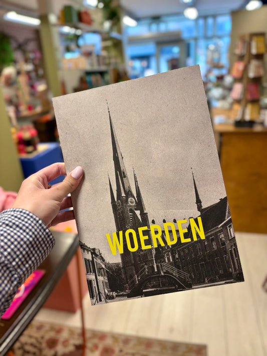 Op de foto zie je een hand die een poster vasthoudt met daarop en kerk en in gele letters 'Woerden'.