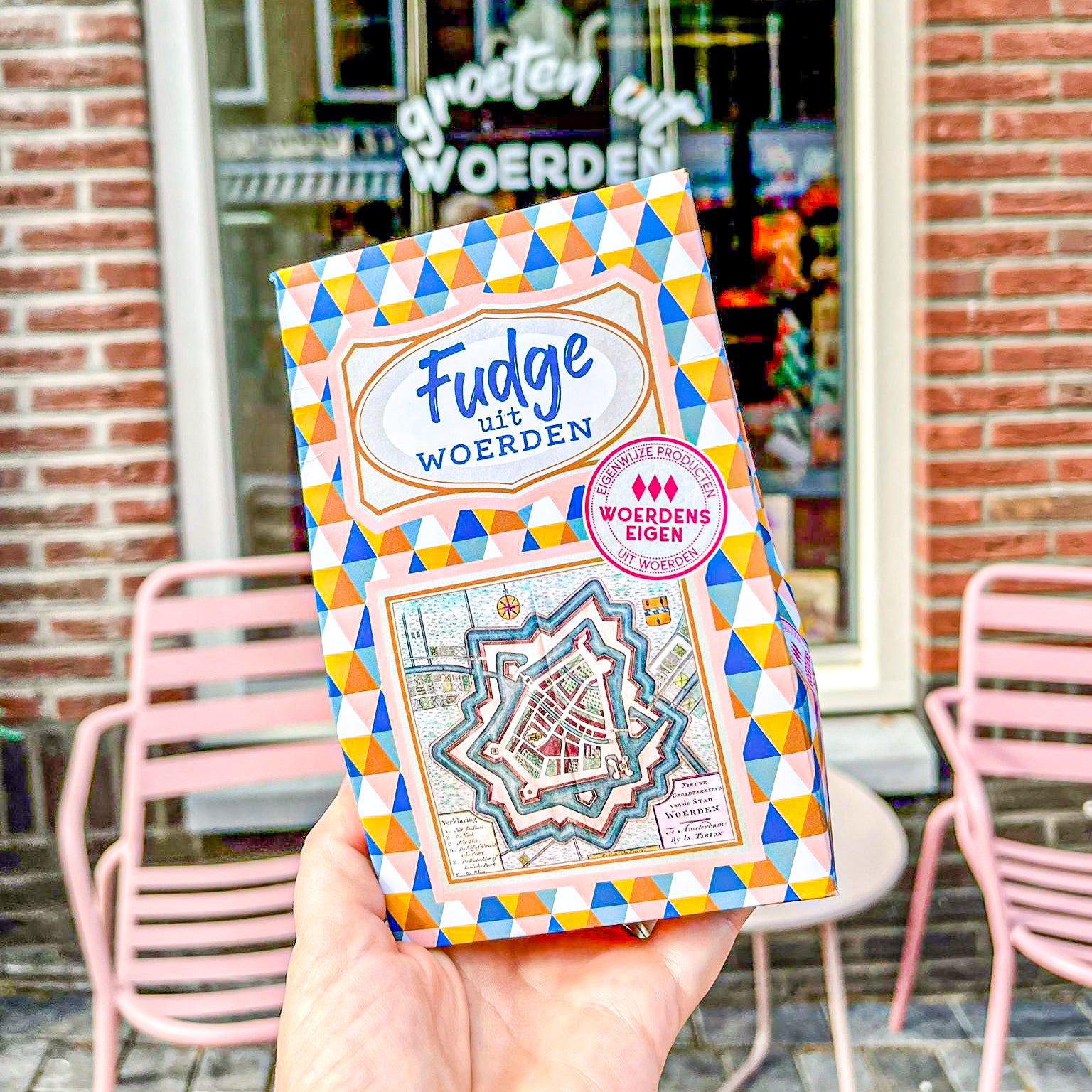 Op de foto zie je een gekleurd doosje met ruitjes erop. Er staat ook een tekst op met 'Fudge uit Woerden'.