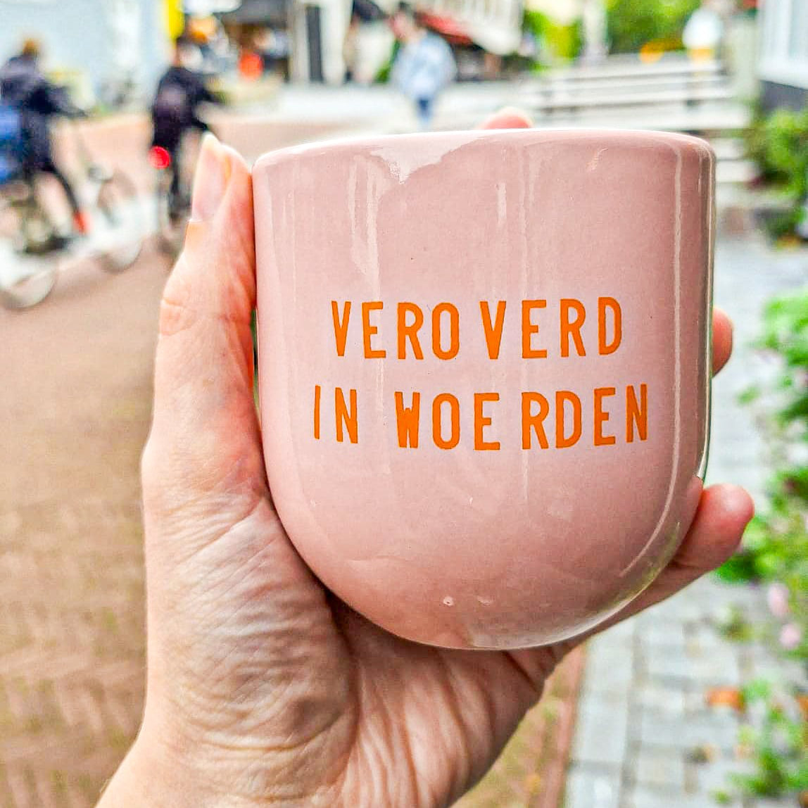 een hand die een roze mok met de opdruk 'veroverd in Woerden' vasthoudt