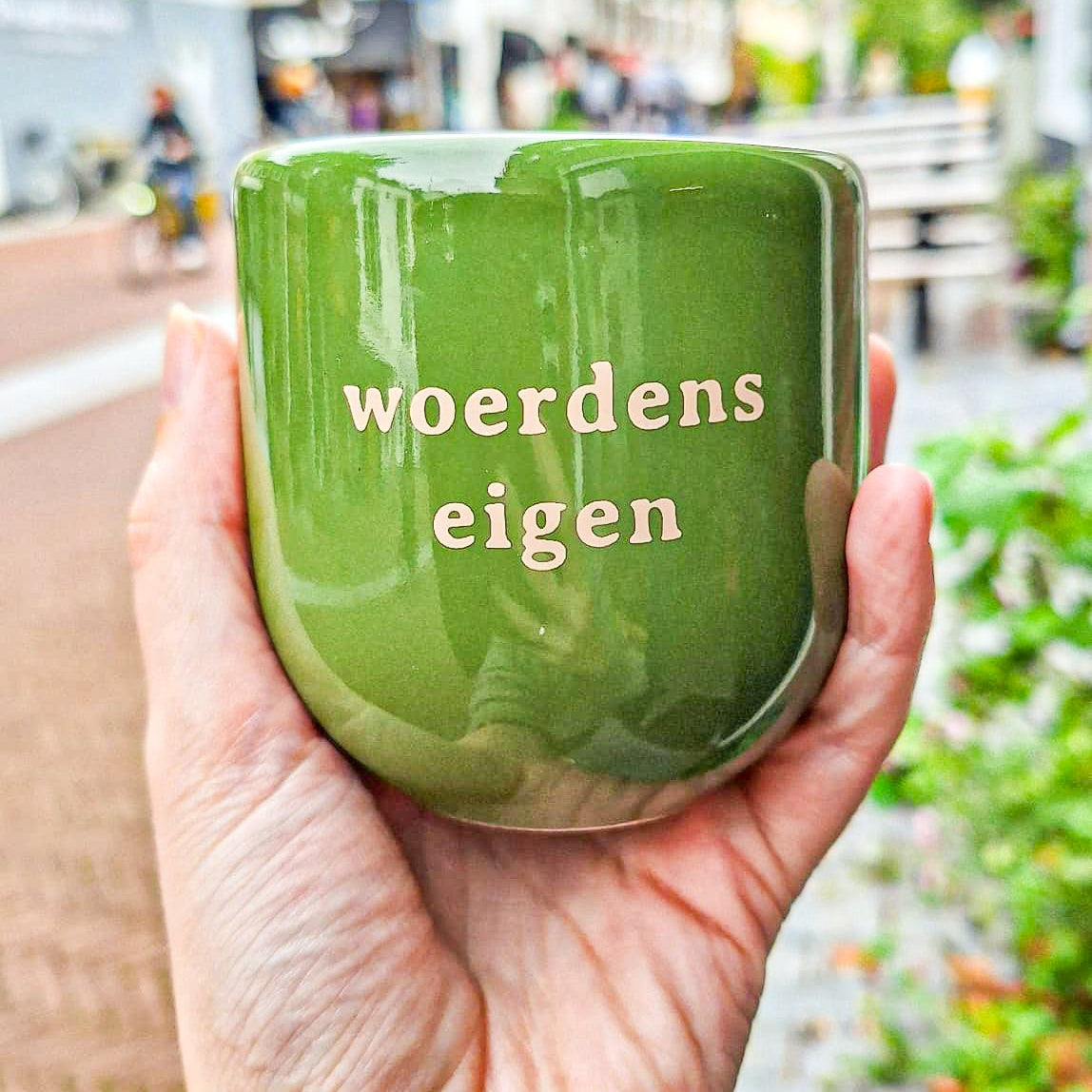 een hand die een groene mok vasthoudt met de opdruk 'Woerdens eigen'